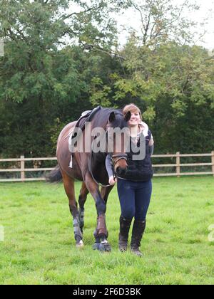 Une jeune femme marche son cheval vers l'appareil photo alors qu'il est encore mis à la porte. Banque D'Images