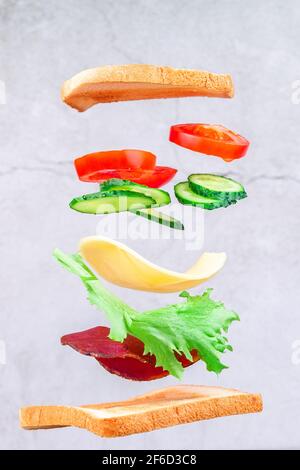 Des couches volantes de sandwich avec du jambon, du fromage et des légumes sur fond de bois. Concept de la nourriture pour le petit déjeuner Banque D'Images