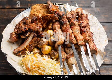 Assortiment de viandes grillées délicieuses sur brochettes avec légumes frais et pommes de terre cuites au four Banque D'Images