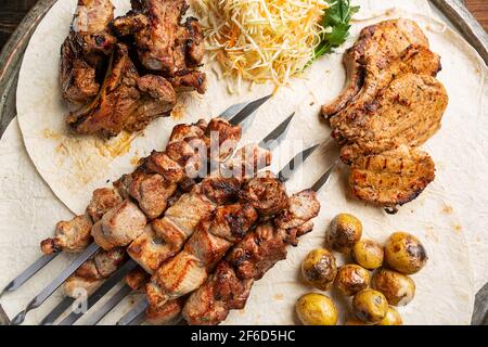 Assortiment de viandes grillées délicieuses sur brochettes avec légumes frais et pommes de terre cuites au four Banque D'Images
