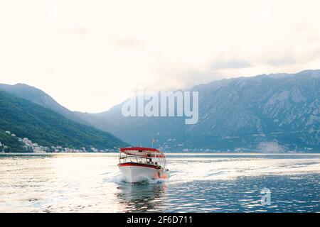 Un bateau à moteur de plaisance avec un auvent au soleil flotte sur les eaux de la baie de Kotor dans la ville de Perast. Banque D'Images