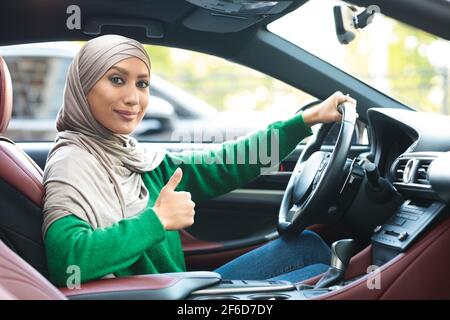 Femme musulmane souriante au volant, montrant les pouces vers le haut Banque D'Images