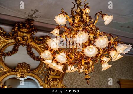 Grand lustre doré avec des tons floraux et des ampoules de style floristique. Sur le fond d'un miroir ancien avec un cadre sculpté doré. Banque D'Images