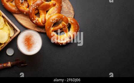 Tasse à bière lager, chips de pommes de terre et bretzel maison frais cuit avec sel de mer sur table en pierre. Collation classique à la bière. Vue de dessus du plan de travail avec espace de copie Banque D'Images