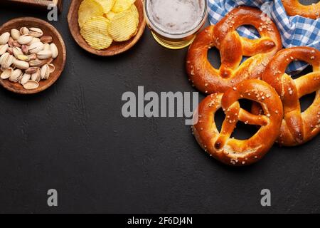 Tasse à bière lager, noix, chips de pomme de terre et bretzel maison frais cuit avec sel de mer sur table en pierre. Collation classique à la bière. Vue de dessus plat avec bac à papier Banque D'Images