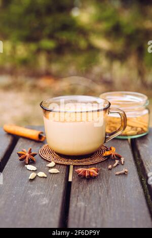 Boire Chai latte au pique-nique en plein air concept. Tasse de chai latte chaud sur table de pique-nique au camping, pot avec mélange d'épices sur fond. Banque D'Images