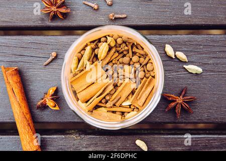 Divers ingrédients du thé de chai faits maison dans un pot en verre, vue sur la pose à plat. Gousses de cardamome vertes, bâtonnets de cannelle, clous de girofle, anis étoilé. Vue ci-dessus. Banque D'Images