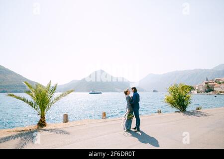 La mariée présente une robe grise élégante et un marié qui s'embrasse La jetée près de la vieille ville de Perast Banque D'Images