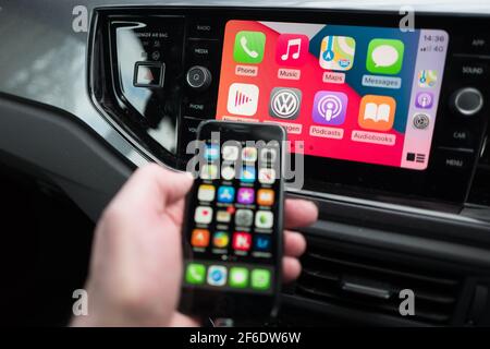 Un homme utilisant son Apple iphone se connecte aussi à l'unité de divertissement et de communication dans un VW Polo. Banque D'Images