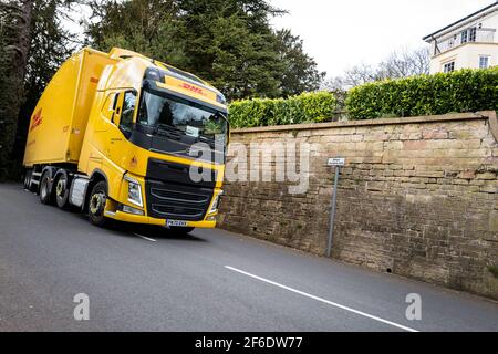 Le camion lourd Volvo FH de DHL, de couleur jaune, conduit le long d'une voie étroite de campagne. Banque D'Images