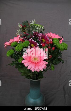 Bouquet de fleurs fraîches et colorées dans de l'argile de forme élégante vase isolé sur fond de tissu gris Banque D'Images