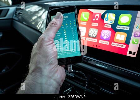 Un homme utilisant son Apple iphone se connecte aussi à l'unité de divertissement et de communication dans un VW Polo. Banque D'Images