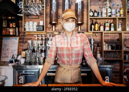 Le travail d'un barman au moment de la couronne. Portrait d'une femme avec un masque debout dans un bar et portant un masque facial. Elle s'attend à o Banque D'Images