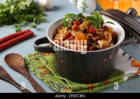 Ragoût de légumes avec saucisses de chasse dans un pot en céramique sur fond bleu clair. Gros plan Banque D'Images