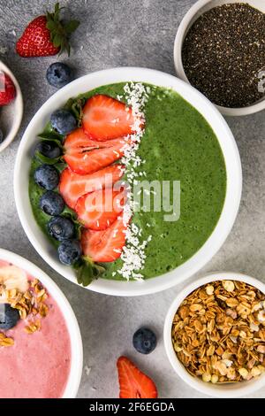 Matcha thé vert petit-déjeuner smoothies saladiers nappés de fraises, bleuets, flocons de noix de coco Overhead, vue de dessus, plat Banque D'Images