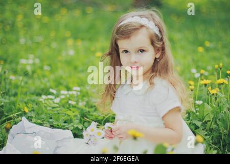 Une fille en robe tient un bouquet de pâquerettes dedans jardin de cerisiers de printemps Banque D'Images