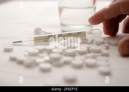 Thermomètre médical, avec une température de 37 degrés dans une pile de pilules, sur le fond d'une main et d'un verre d'eau. Banque D'Images