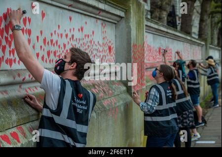 Londres, Royaume-Uni. 31 mars 2021. Le mur national du Covid Memorial à l'extérieur de l'hôpital St Thomas, sur la rive sud. La famille et les amis de quelques-uns des plus de cent quarante-cinq mille personnes qui ont perdu la vie à Covid-19 attirent le cœur à la main sur un mur en face du Parlement de Londres. Chaque cœur représente quelqu'un qui était aimé. Quelqu'un qui a été perdu trop tôt à Covid-19. Ils organisent ce mémorial temporaire car "ils ne croient pas que c'est à ceux qui ont dirigé la réponse de ce pays à Covid-19 de décider comment nous nous en moquons". Une fois installés, ils gardera le mémorial Banque D'Images