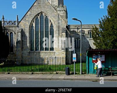 Femme de sureau attendant à l'arrêt de bus en face de l'église, dans le village de Hemingbrough, East Yorkshire, Angleterre Royaume-Uni Banque D'Images