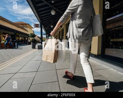 Vue arrière d'une femme seule marchant sur l'allée avec Plusieurs magasins au Roppenheim, le style de la boutique de papier de conservation Sacs à Aigle et autres marques Banque D'Images