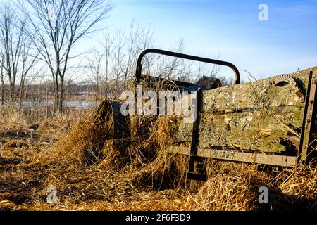 Un morceau abandonné d'équipement agricole antique, un épandeur de fumier tiré par des chevaux, se trouve dans un état de déréparation. La machine à panne est recouverte d'un vieux gr Banque D'Images