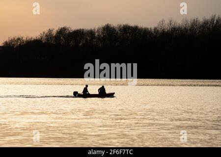 les gens dans la silhouette de bateau à grande vitesse au coucher du soleil sur le lac avec lumière dorée reflétant sur l'eau de la rivière voile rapidement pour sauver les nageurs. Réservoir eau calme Banque D'Images