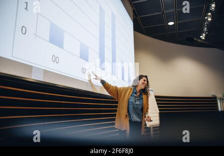 femme d'affaires faisant des gestes à l'écran de projection et faisant une présentation pendant le séminaire. Conférencière faisant une présentation en conférence. Banque D'Images