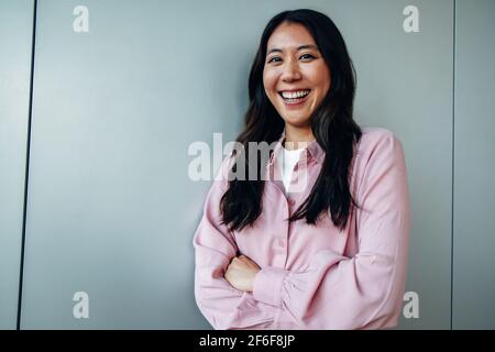 Portrait d'une belle jeune femme d'affaires souriant au bureau. Femme de direction qui se contente de se trouver contre un mur. Banque D'Images