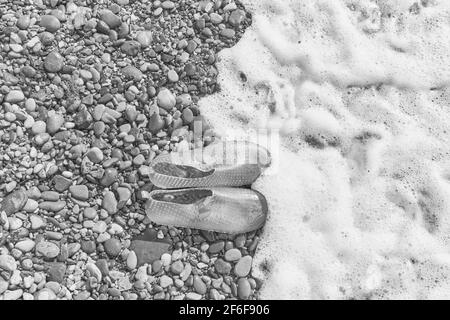 Pantoufles en caoutchouc bleu pour femmes pour nager sur une plage de galets avec un moussage de mer. Vue de dessus Banque D'Images