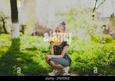 Une fille en robe sniffs un bouquet de pissenlits jaunes dans le jardin de cerisier de printemps Banque D'Images