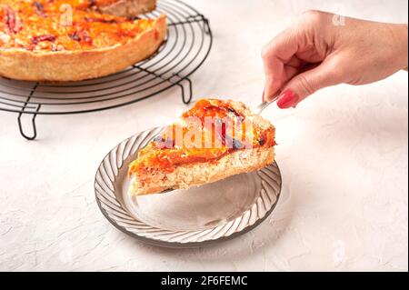 La main de la femme tient sur un morceau de tarte à la quiche maison avec du poulet, des tomates séchées, du fromage cheddar sur une assiette en céramique Banque D'Images