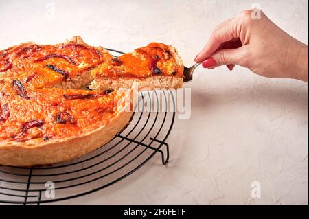 La main de la femme tient sur un morceau de tarte à la quiche maison avec du poulet, des tomates séchées, du fromage cheddar sur une assiette en céramique Banque D'Images