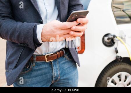 Homme d'affaires utilisant un téléphone portable sur l'arrière-plan de charge de la voiture électrique au point de charge Banque D'Images