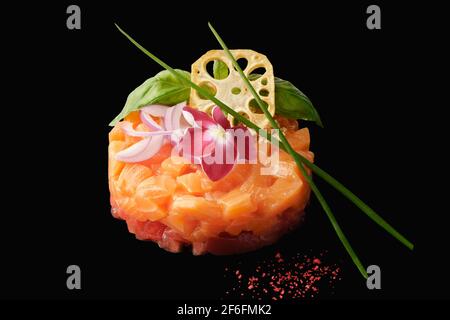 Tartare de saumon à la tomate, oignon rouge, ail, basilic, câpres, racine de lotus, tobiko caviar, citron, ciboulette. Isolé sur fond noir Banque D'Images