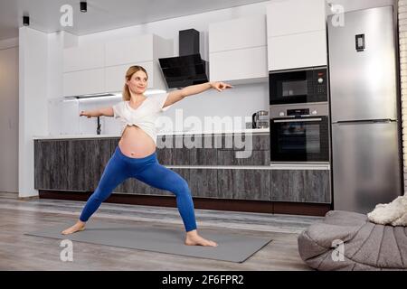 Jeune femme enceinte pieds nus dans les jambes et t-shirt étirant les jambes tout en faisant des exercices de yoga pendant l'entraînement à la maison, étirant le corps Banque D'Images