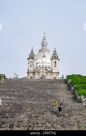 Jeune homme portant son vélo sur ses épaules tout en montant des escaliers pour une courte coupe dans le sanctuaire de Sameiro à Braga, Portugal. Banque D'Images