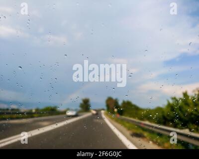 Conduite sur route italienne sous la pluie avec arc-en-ciel. Gouttes de pluie sur le pare-brise et paysage nuageux avec flou en arrière-plan. Vue panoramique en Italie près de NAPL Banque D'Images