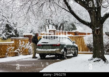 Homme d'âge moyen avec voiture couverte de neige dans l'allée journée très enneigée avec chute de neige Banque D'Images