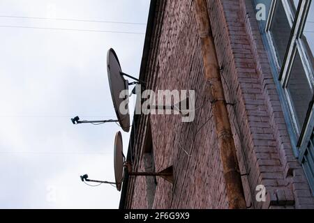 Antenne de télévision par satellite rouillée - plat sur le mur de brique rouge du bâtiment. Photo sur l'arrière-plan du ciel bleu. Banque D'Images