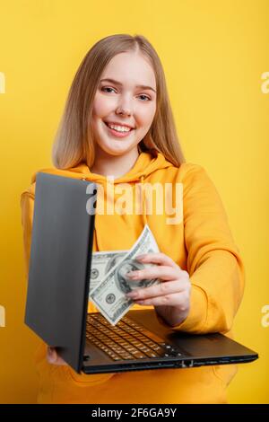 Belle jeune femme freelance prend des billets d'argent de dollars de portable. Gagner dans la richesse de jeu de casino en ligne par travail de freelance. INFORMATIQUE travail à distance vi Banque D'Images