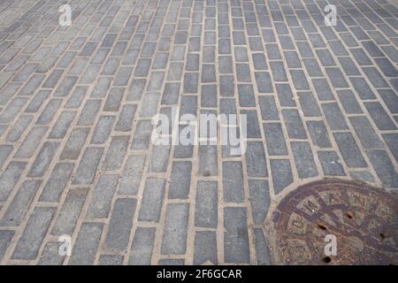 passerelle de la rue de la ville avec ancien trou d'homme de grunge couvre brique pavée rue en forme de forme Banque D'Images