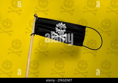 Le masque médical vole un drapeau pirate sur un poteau avec le crâne COVID et les os. Masque noir sur fond jaune texturé. Drapeau d'attaque du virus pirate noir. C Banque D'Images