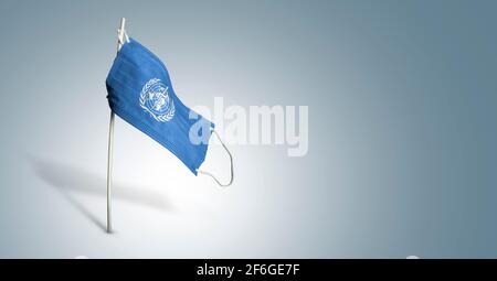 Masque de l'Organisation mondiale de la Santé sur fond bleu clair. Drapeau agitant de L'OMS peint sur le masque médical sur le poteau. Indicateur d'attaque de virus. Concept de la bannière Banque D'Images