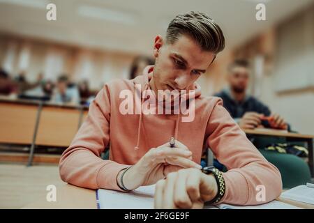 un jeune étudiant utilise une montre intelligente de tricherie dans un cours de mathématiques à l'université Banque D'Images