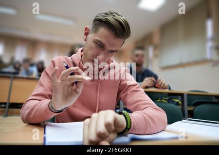 un jeune étudiant utilise une montre intelligente de tricherie dans un cours de mathématiques à l'université Banque D'Images