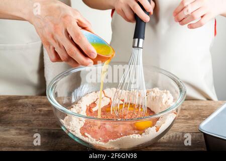 Mère et fille cuisant ensemble dans le concept de cuisine avec la fille tenant un fouet et la femme versant soigneusement du beurre fondu ou du jaune d'œuf Banque D'Images