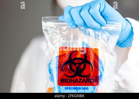 Une femme chercheuse porte un sac en plastique transparent avec le logo de risque biologique imprimé. Le sac contient des échantillons biologiques potentiellement dangereux. Scient Banque D'Images