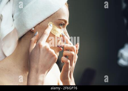 La femme caucasienne se concentre sur l'application de cellules oculaires hydrogel sous les yeux à la maison ayant une journée au spa Banque D'Images