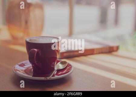 Gros plan Latte art chaud, Cappuccino café dans une tasse rouge sur une table en bois dans un café arrière-plan flou avec le processus d'image bokeh avec style vintage Banque D'Images