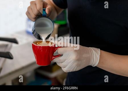 Gros plan Barista verser du lait chaud dans une tasse de café pour préparer un délicieux latte, cappuccino art Rosetta. Fermez les mains du barista en versant du lait chaud Banque D'Images